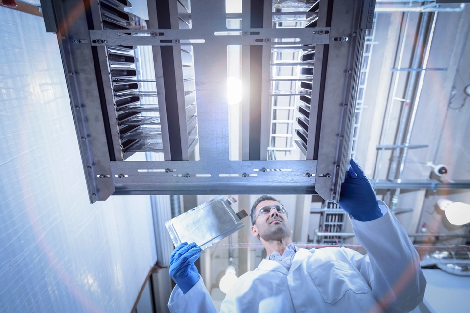 Scientist with lithium ion pouch cell manufacture machine in battery research facility, low angle view