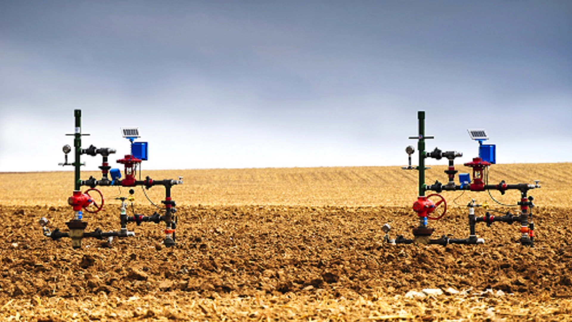 Natural gas wellheads in a plowed cornfield.
