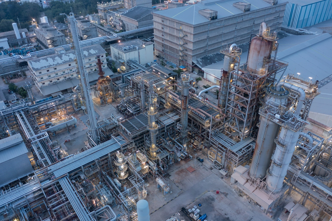 Twilight descends on a sprawling chemical facility, its network of pipes and reactors illuminated, signifying relentless production.