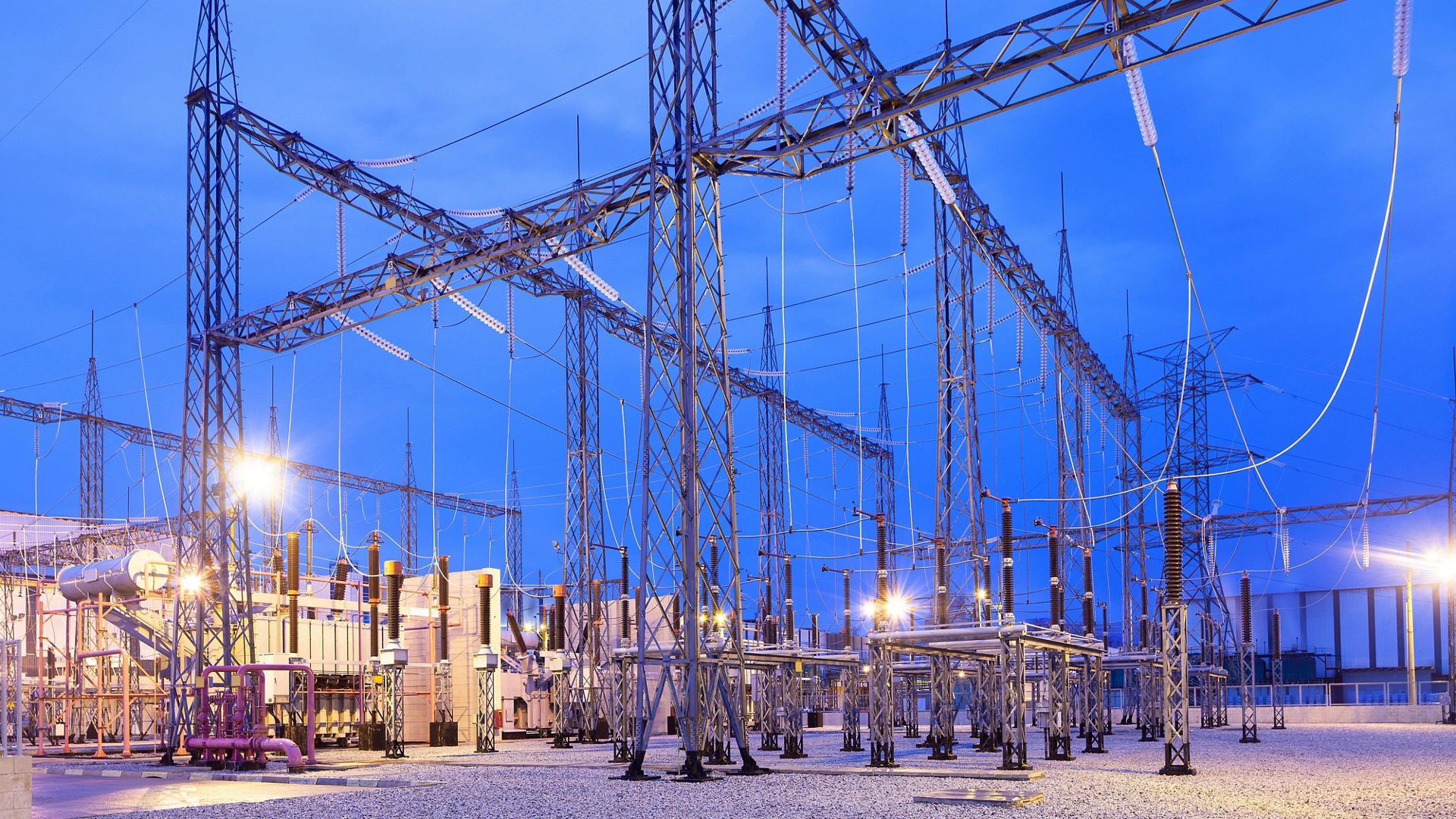 Illuminated electricity substation at dusk.