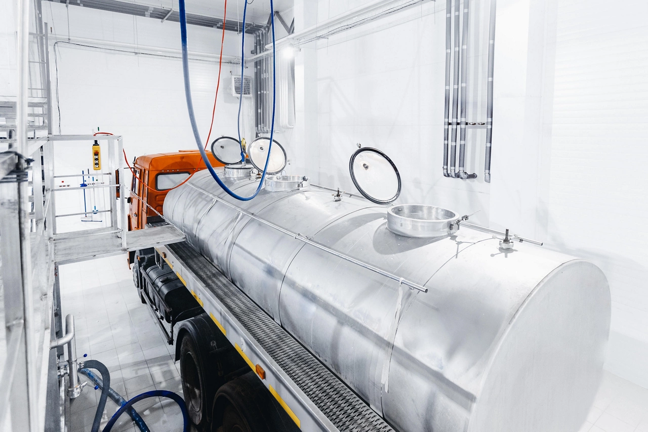 Milk tanker truck pumps products into steel storage tanks, dairy factory industry.